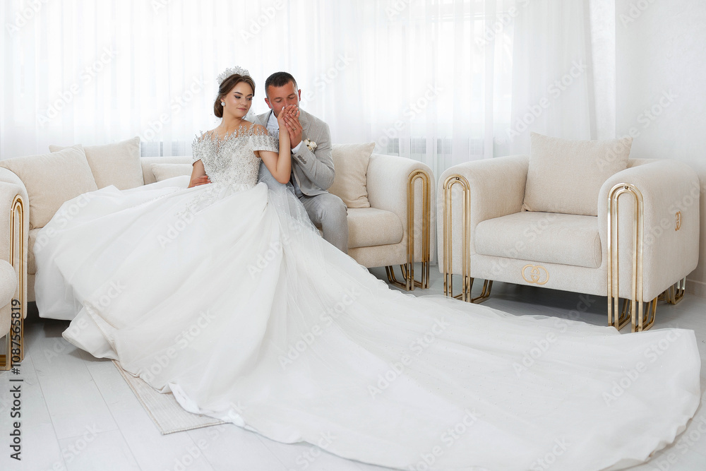 A bride and groom are sitting on a couch in a room with a large white couch in the background