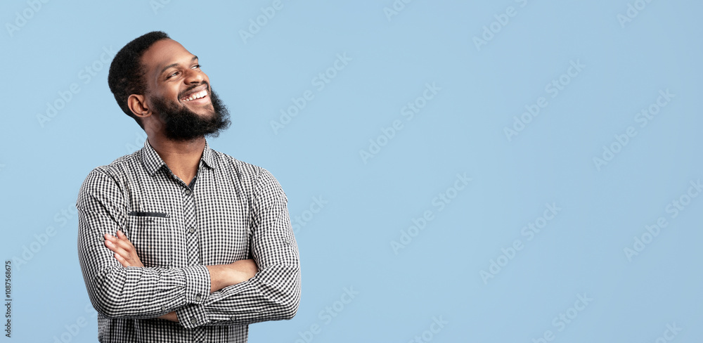 Confident Person. Portrait of cheerful handsome young black male model standing isolated on blue studio background looking aside at copy space. Laughing african american man with folded arms Confident Person. Portrait of cheerful handsome young black male model standing isolated on blue studio background looking aside at copy space. Laughing african american man with folded arms
