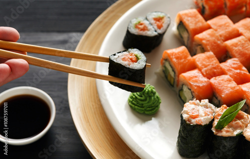 Eating roll sushi in japanese restaurant, hand with chopsticks closeup. Female has dinner photo