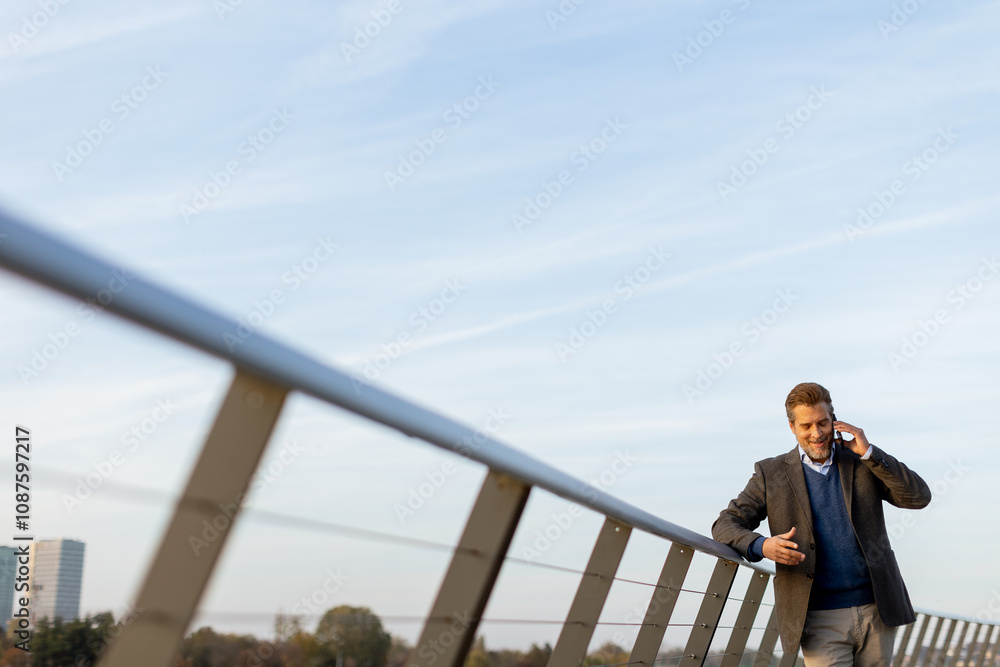 A businessman walking on a modern bridge in the city while talking on his phone during a clear afternoon A businessman walking on a modern bridge in the city while talking on his phone during a clear afternoon