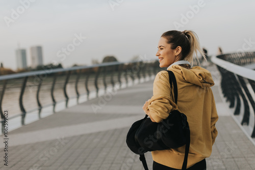 A young woman in a bright yellow hoodie enjoys an evening stroll along a picturesque riverside walkway photo