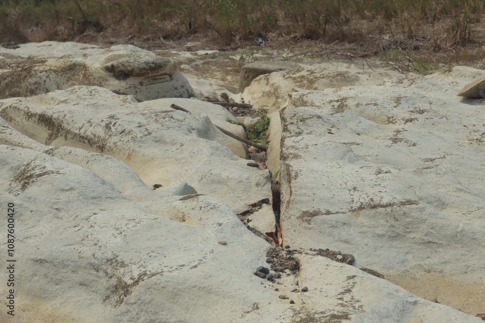 A dry riverbed showcases a unique texture of white, eroded rocks with natural indentations and pebbles scattered between A dry riverbed showcases a unique texture of white, eroded rocks with natural indentations and pebbles scattered between