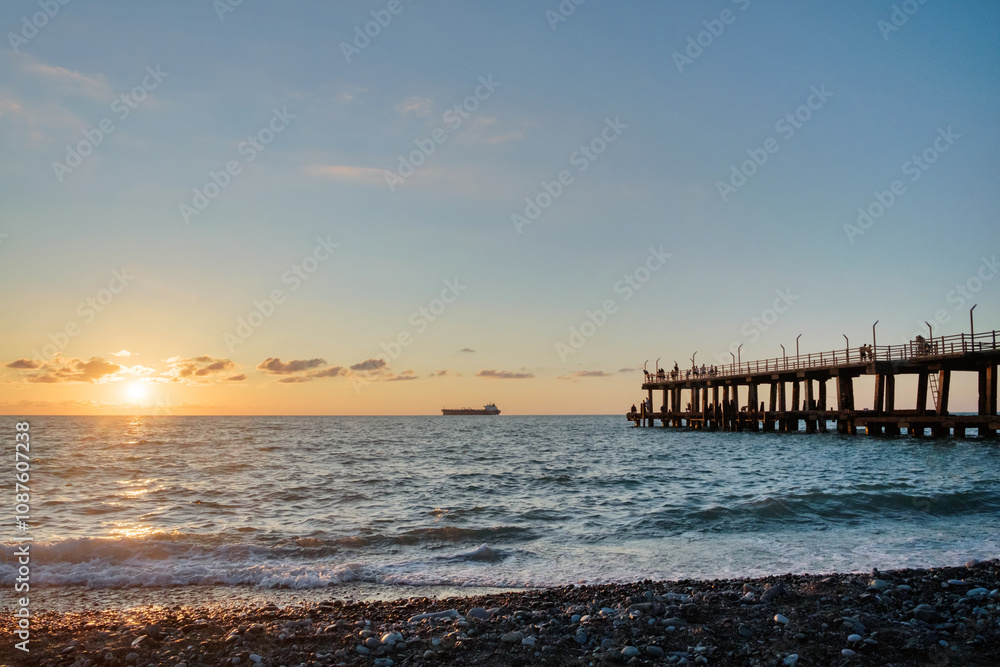 A sunset on the beach with crowded pier and a ship on horizon A sunset on the beach with crowded pier and a ship on horizon