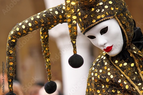 A close-up of a masked performer at the Venetian Carnival, wearing a sparkling gold and black jester costume.