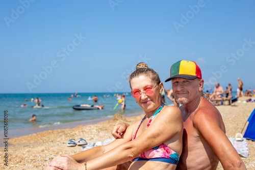 Happy Man and woman of mature age smiling in swimsuit sitting on seashore. Vacation at sea