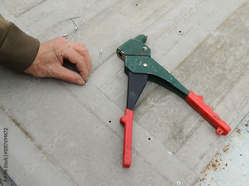 riveting tool on iron texture top view and male hand holding aluminum rivet, hand held device for setting rivets when joining thin metal parts