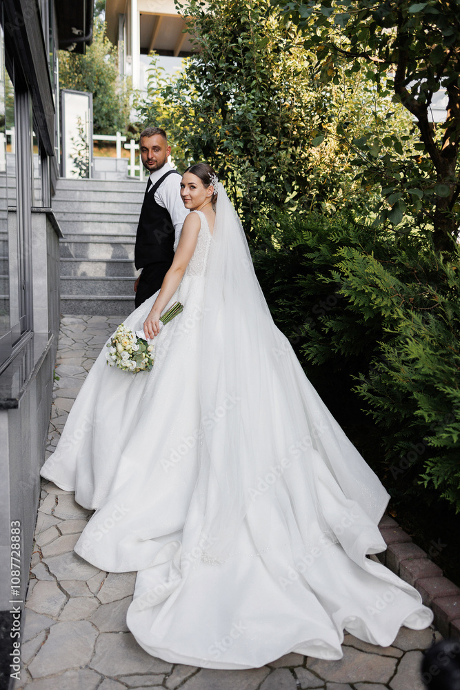 A bride and groom are posing for a picture on a staircase. The bride is wearing a white dress and holding a bouquet, while the groom is wearing a black vest. Concept of love and happiness A bride and groom are posing for a picture on a staircase. The bride is wearing a white dress and holding a bouquet, while the groom is wearing a black vest. Concept of love and happiness