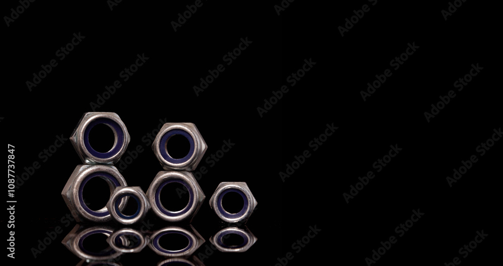 Steel nuts of different sizes on black background with reflecting dark surface. Close up macro shot with copy space Steel nuts of different sizes on black background with reflecting dark surface. Close up macro shot with copy space