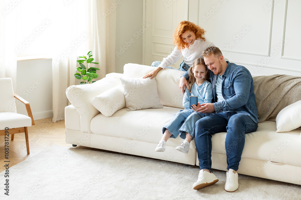 Positive parents and their child girl taking family selfie, using cellphone sitting on comfortable couch, leisure time with family, free space Positive parents and their child girl taking family selfie, using cellphone sitting on comfortable couch, leisure time with family, free space