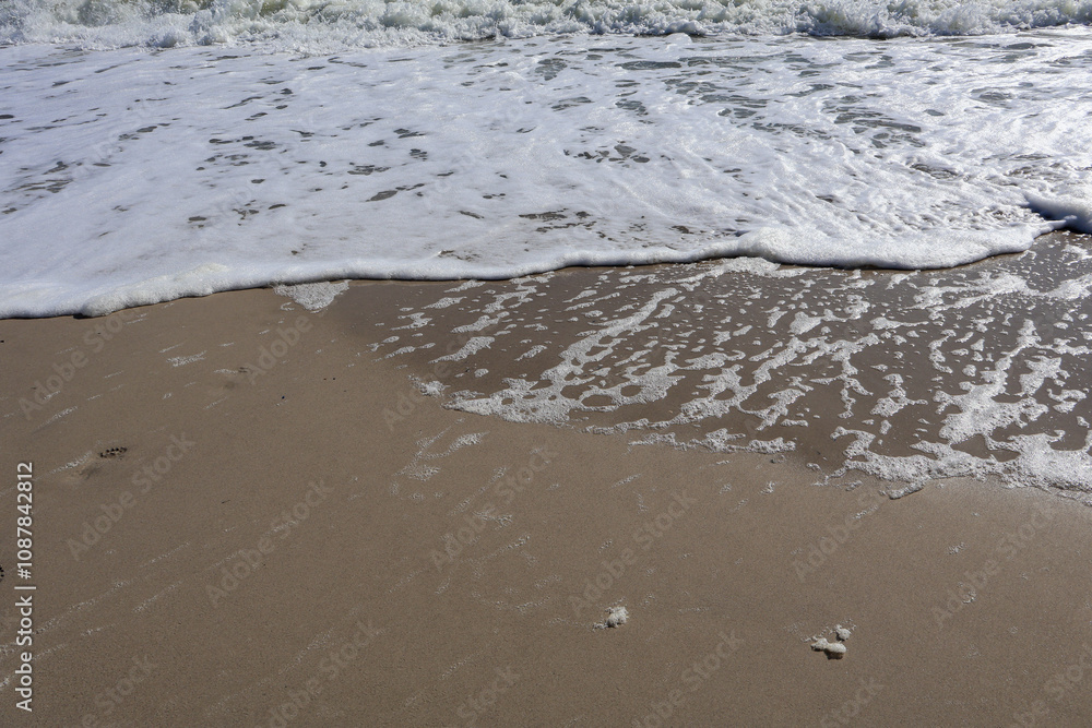 Close-up view of gentle ocean waves creating foam patterns as they meet the sandy beach, reflecting sunlight for a serene coastal scene. Close-up view of gentle ocean waves creating foam patterns as they meet the sandy beach, reflecting sunlight for a serene coastal scene.