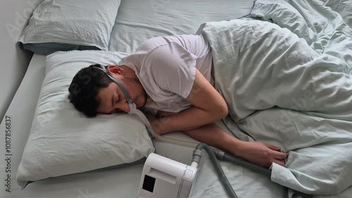 A man in his mid-thirties with sleep apnea disorder, sleeps using a nasal mask and CPAP device in a bed.
