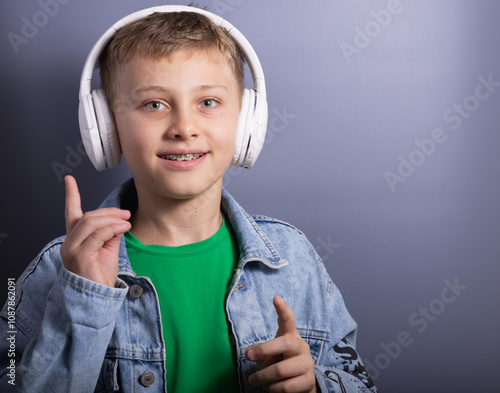 boy teenager with dental braces, listening music in wireless headphones isolated on grey background