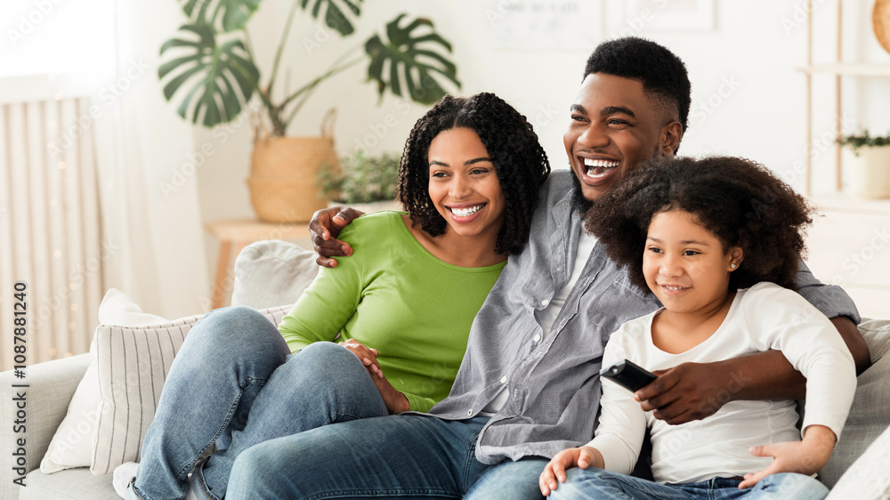 Black family of three relaxing on couch, watching tv together, enjoying spending time at home, resting in living room, free space Black family of three relaxing on couch, watching tv together, enjoying spending time at home, resting in living room, free space