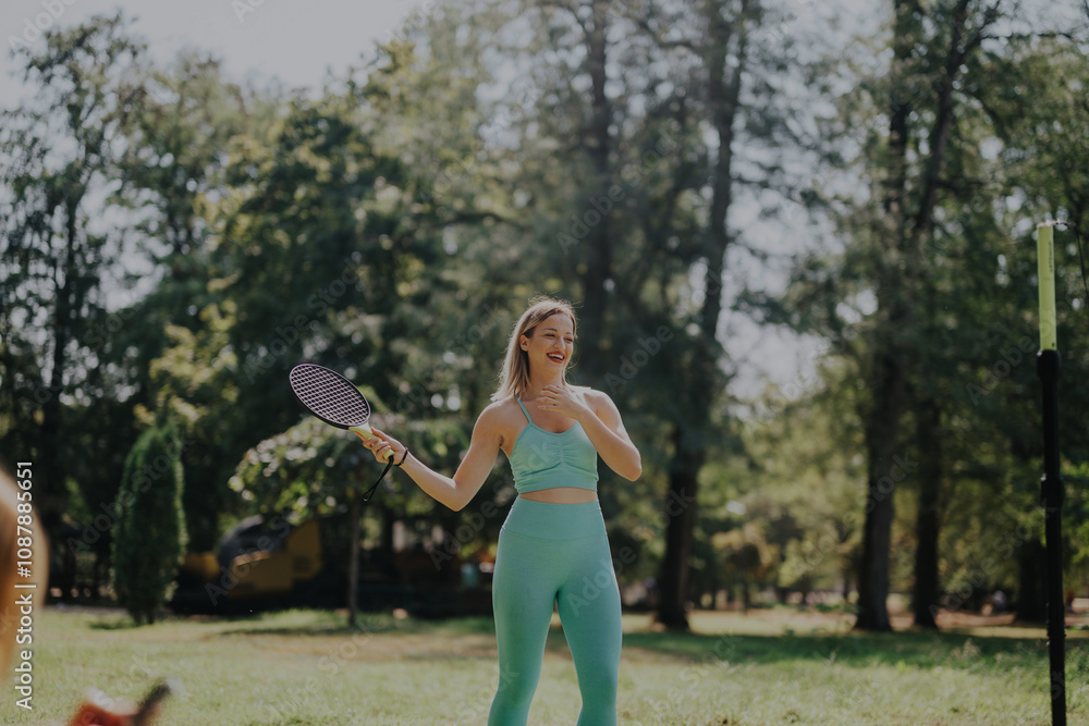 A joyful woman in athletic wear enjoys a game of badminton with friends in a sunny park setting. The vibrant greenery and casual atmosphere highlight a fun and active outdoor scene. A joyful woman in athletic wear enjoys a game of badminton with friends in a sunny park setting. The vibrant greenery and casual atmosphere highlight a fun and active outdoor scene.