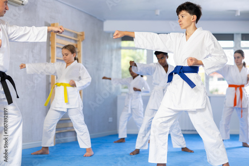 Determined boy in white kimono practicing punches in gym during martial arts workout with multiracial group of tweens. Shadow fight, combat sports training concept