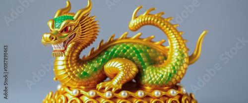 A striking golden dragon statue resting on a golden base. The dragon, adorned with vibrant green scales, is elegantly curled up, radiating a sense of power and grace.