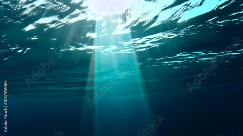 An ethereal aquatic world unfolds as sunlight slices through pristine turquoise seas. Radiant beams cast magical glow, descending beneath soft surface undulations into deeper water expanses.
