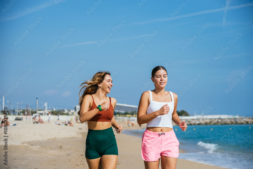 Two young women running and smiling on the beach on a sunny day Two young women running and smiling on the beach on a sunny day