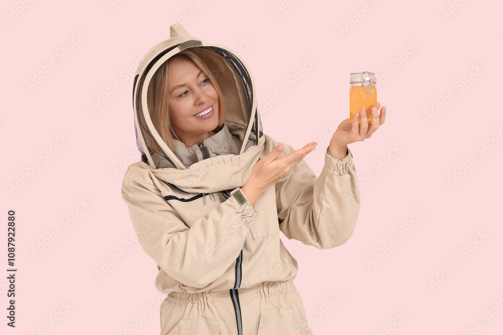 Female beekeeper pointing at jar of sweet honey on pink background Female beekeeper pointing at jar of sweet honey on pink background