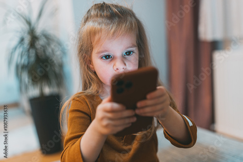 Φωτογραφία A girl intently observes a smartphone, illustrating deep concentration and interaction with technology, against a calm indoor setting with subtle lighting