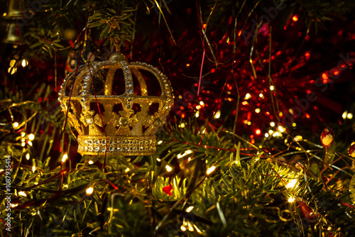 A royal crown Christmas tree decoration with sparkling jewels and  red and gold tinsel and lametta background. Fairy lights on festive tree.