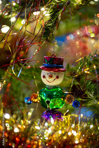 Festive snowman clown Christmas tree ornament with bells. Festive decoration with gold and red lametta, tinsel and fairy lights.