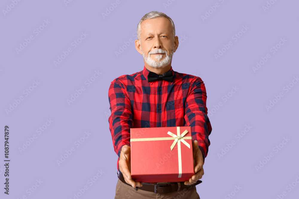 Handsome happy mature man with stylish bow tie and gift box on purple background Handsome happy mature man with stylish bow tie and gift box on purple background