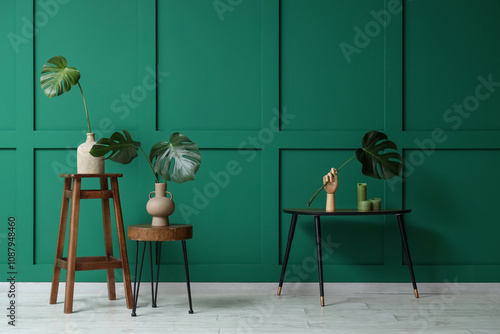 Vases and wooden hand with monstera leaves on tables near green wall