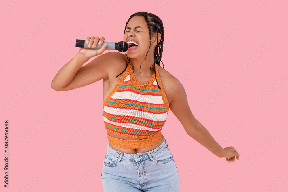 Young African-American woman with microphone singing on pink background Young African-American woman with microphone singing on pink background