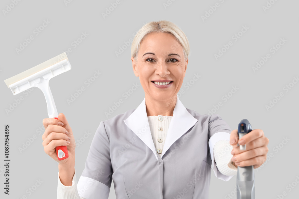 Middle-aged chambermaid with sprayer bottle and squeegee on grey background Middle-aged chambermaid with sprayer bottle and squeegee on grey background