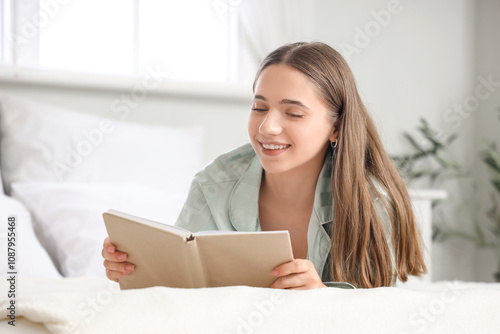 Young pretty woman in pajamas reading book on bed at home