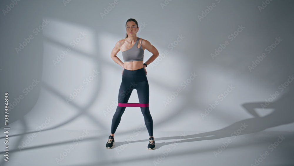 Sportswoman using fitness band at empty room. Woman performing exercise for leg