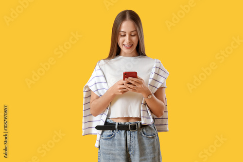 Young woman using mobile phone on yellow background