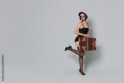 Pin-up woman with suitcase on grey background photo