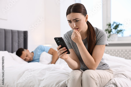 Fotografija Nervous woman checking husband's smartphone while he sleeping in bedroom, select