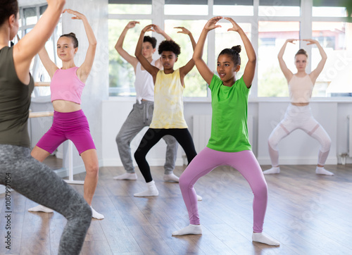 Obraz na plátně Motivated african american teen girl participating in beginner group ballet class, practicing graceful dance movements in sunlit choreography studio