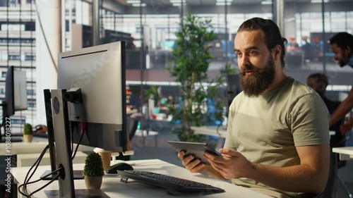 Employee looking at PC monitor, drinking coffee, checking data needed for finding business insights and finishing project task. Man analyzing data on computer, enjoying beverage, camera B photo