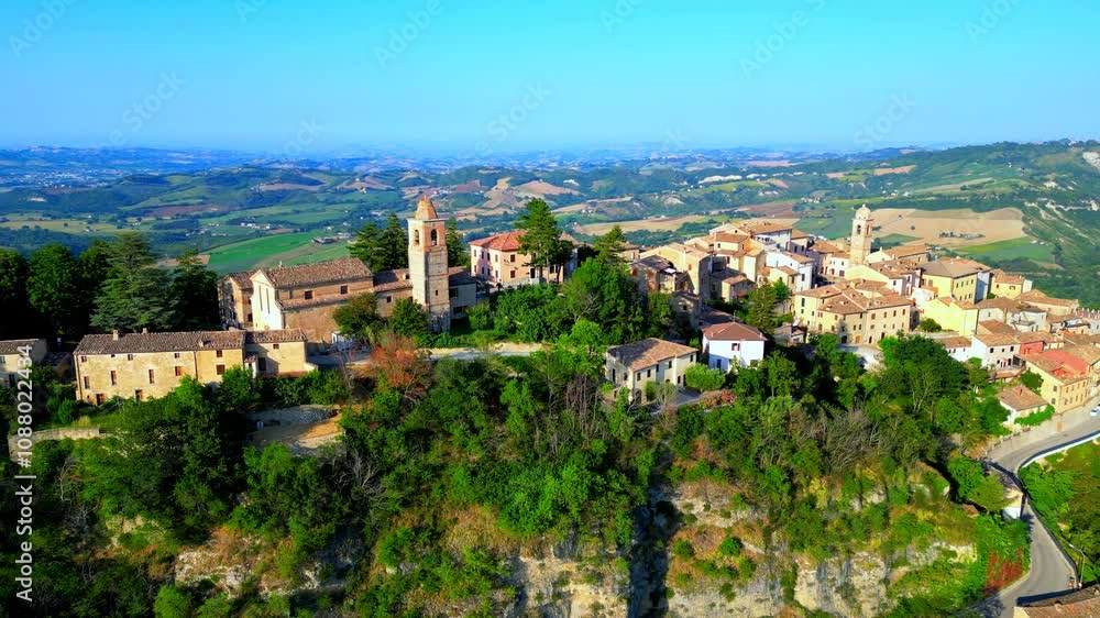 Acrobatic aerial pullback, pedestal up and pan left shot of Monte San Martino with an expanding vision of the perched town, buildings, a park on the left between rich greenery and the hilly background Acrobatic aerial pullback, pedestal up and pan left shot of Monte San Martino with an expanding vision of the perched town, buildings, a park on the left between rich greenery and the hilly background