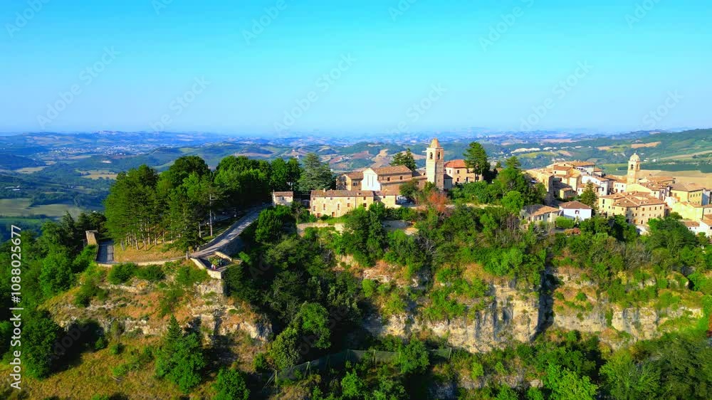 Swift aerial truck right shot of Monte San Martino, a complete overview of the historical town sitting on a vegetation-filled cliff, with white, brown and yellow buildings, churches, belltowers, roads Swift aerial truck right shot of Monte San Martino, a complete overview of the historical town sitting on a vegetation-filled cliff, with white, brown and yellow buildings, churches, belltowers, roads