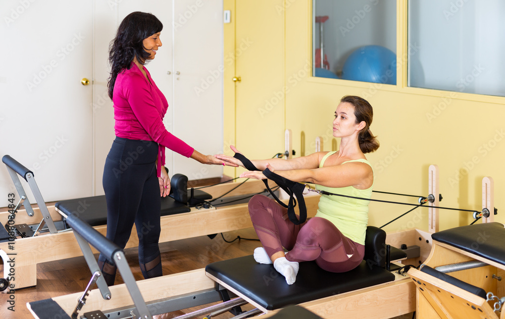 Personal female trainer controlling movements of young woman doing pilates on reformer in fitness studio.. Personal female trainer controlling movements of young woman doing pilates on reformer in fitness studio..