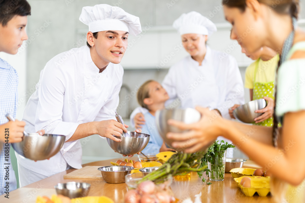 ..Young guy and adult woman chef at master class teaches group of children how to cook food ..Young guy and adult woman chef at master class teaches group of children how to cook food