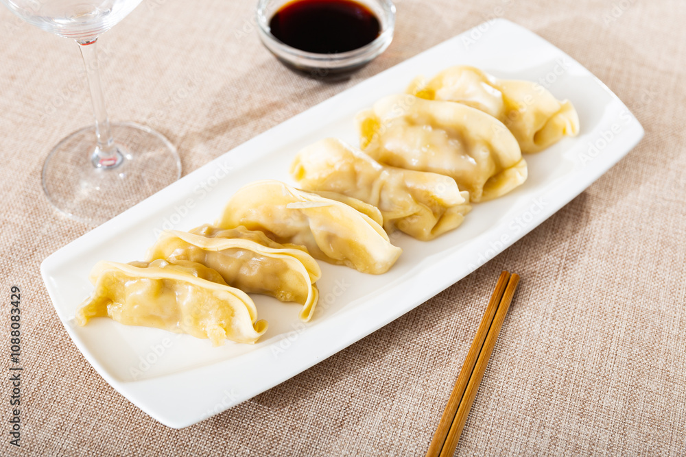 In oriental restaurant, delicious boiled gyoza dumplings, supplemented with necessary chopsticks and spicy soy sauce. Festive dish serving, eating out, concept of tasty, healthy, healthy varied food In oriental restaurant, delicious boiled gyoza dumplings, supplemented with necessary chopsticks and spicy soy sauce. Festive dish serving, eating out, concept of tasty, healthy, healthy varied food