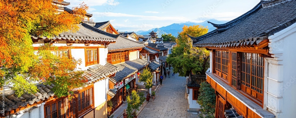 Obraz premium A picturesque old street lined with traditional houses, vibrant foliage, and scenic mountains in the background, capturing the charm of historic architecture.