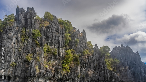 Sheer, inaccessible cliffs against the sky and clouds. There is green tropical vegetation on the steep furrowed slopes. Philippines. Palawan. photo