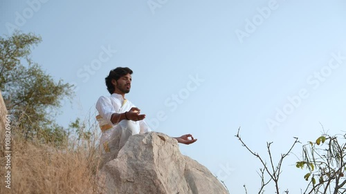 young Indian yogi doing his yoga mediation practices on hills rocks in forest