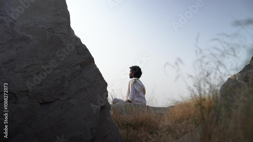 young Indian yogi doing his yoga mediation practices on hills rocks in forest
