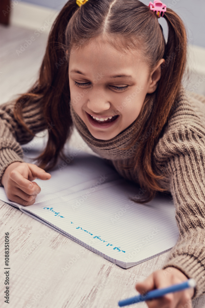 Happy elementary school student writing on notebook at home Happy elementary school student writing on notebook at home