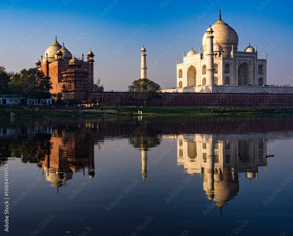 Fototapeta premium The iconic taj mahal and its mirror image on the yamuna river during a tranquil sunrise