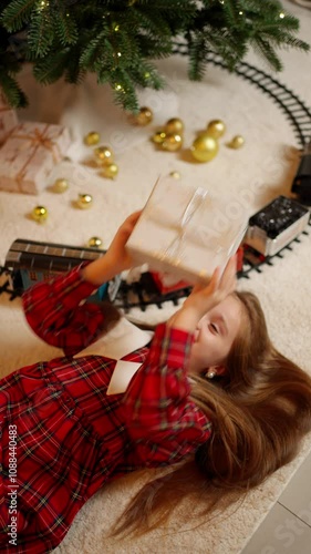 Girl with gift box is lying under Christmas tree. Concept of fabulous new year. photo