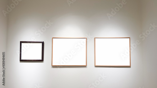 A clean, white gallery wall featuring three frames of varying sizes illuminated by soft lighting, creating a modern and minimalist atmosphere for art or design displays.

